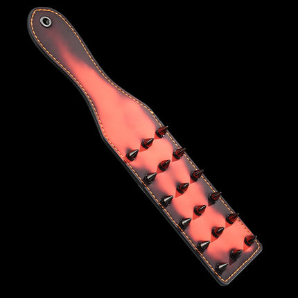 Red heat-reactive leather spanking paddle featuring sharp black metal cone spikes and orange contrast stitching