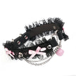 QIYE_Leather_Lilith_Collar_Choker_Heat_Reactive: A stylish choker featuring black lace, pink bows, metallic chains and rings, and a pink bell, in its color before heat - reactive transformation. 
