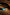 QIYE_Leathers_Heat - Reactive_Collars_Comet_color: A heat - reactive collar placed on a wooden background, featuring black leather with a blue heat - reactive panel, and shiny gold - toned metal chains and clasps.